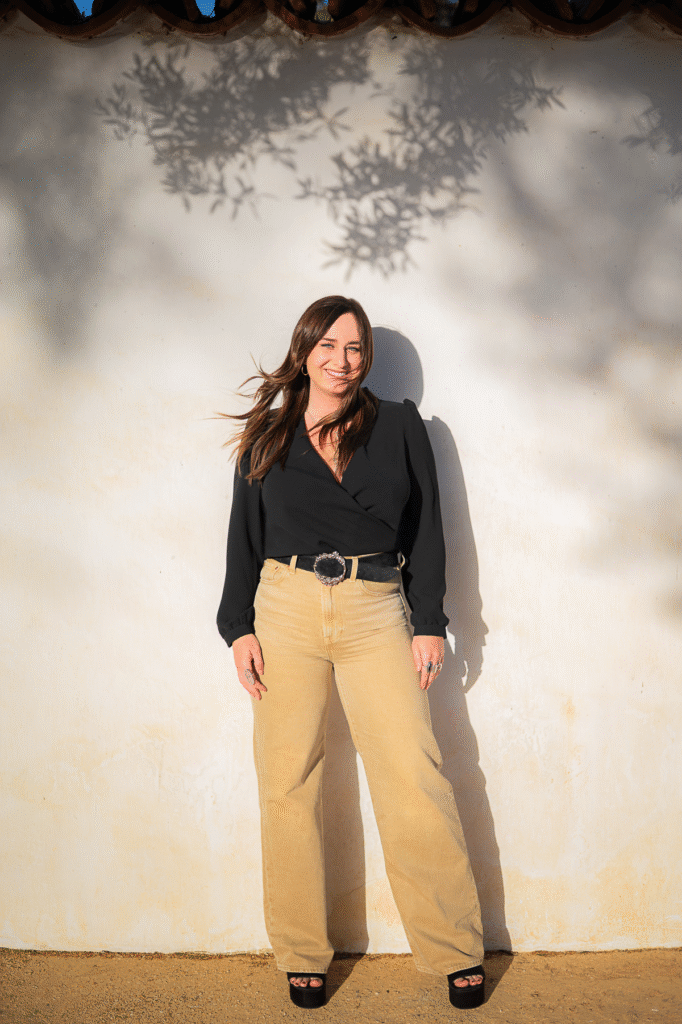 Woman standing against sunlit white wall.
